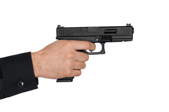 Unrecognizable man pulling trigger, while holding short-barrelled handgun.